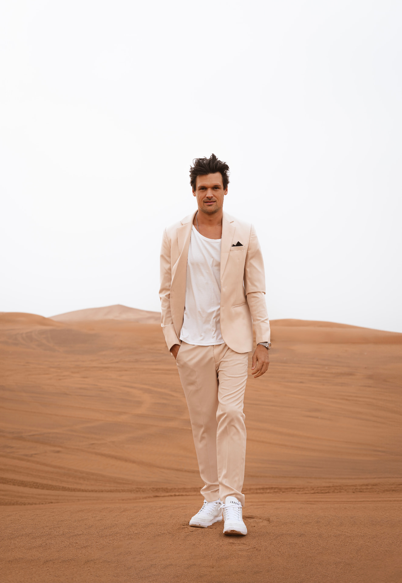 Man in a cream tailored suit walking across desert dunes in Dubai